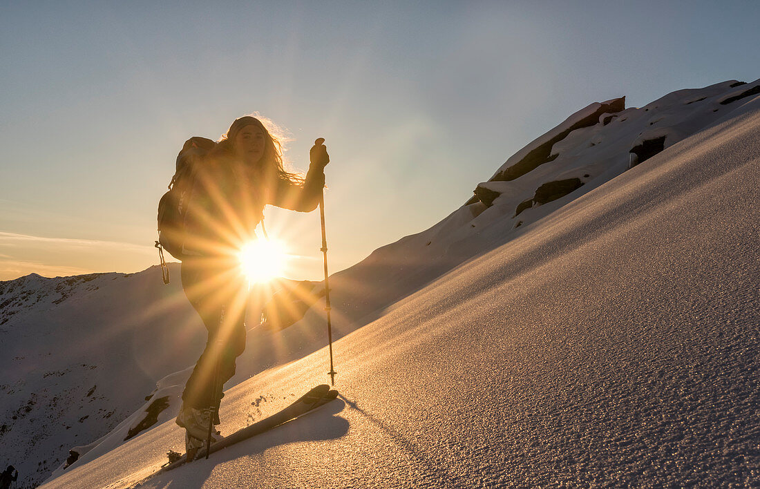 Junge Skitourengeherin spurt durch einen unberührten Hang in warmer Morgensonne, Zischgeles, Sellrain, Tirol, Österreich