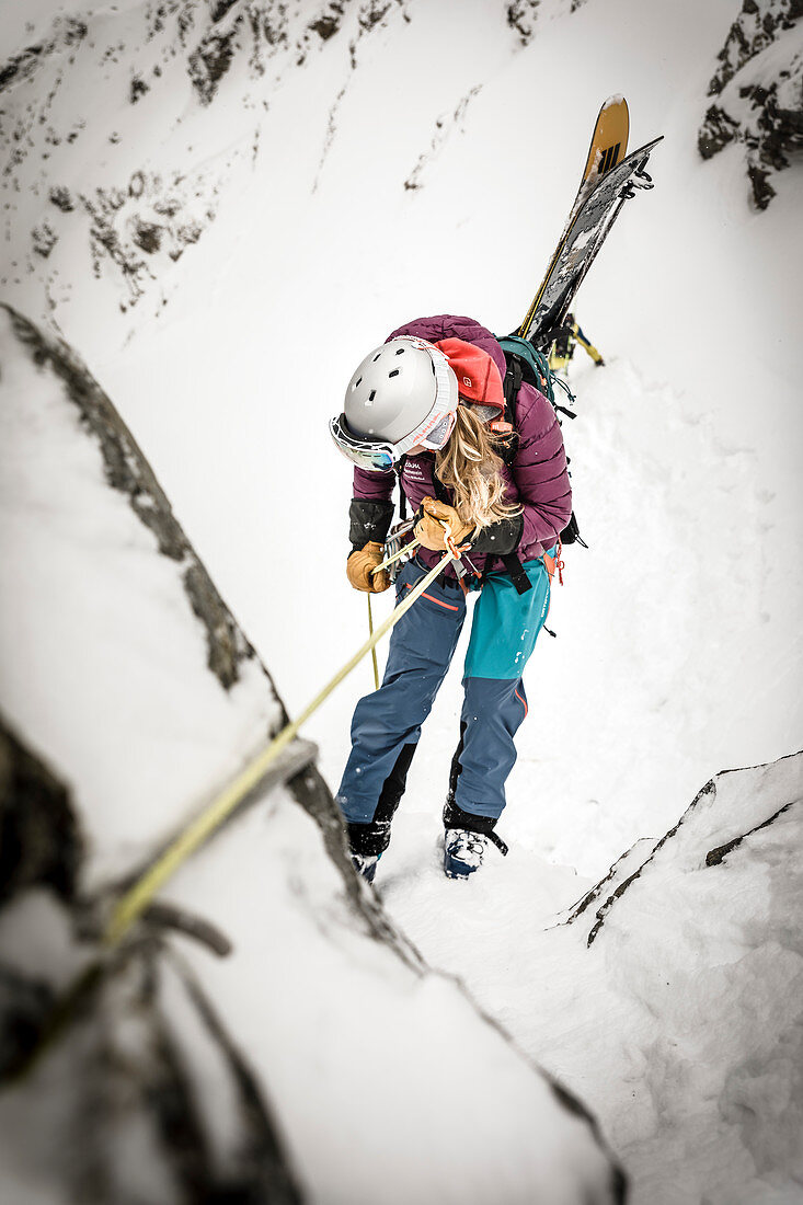 Young woman rappels off a boulder with skis, Stubai Alps, Tyrol, Austria