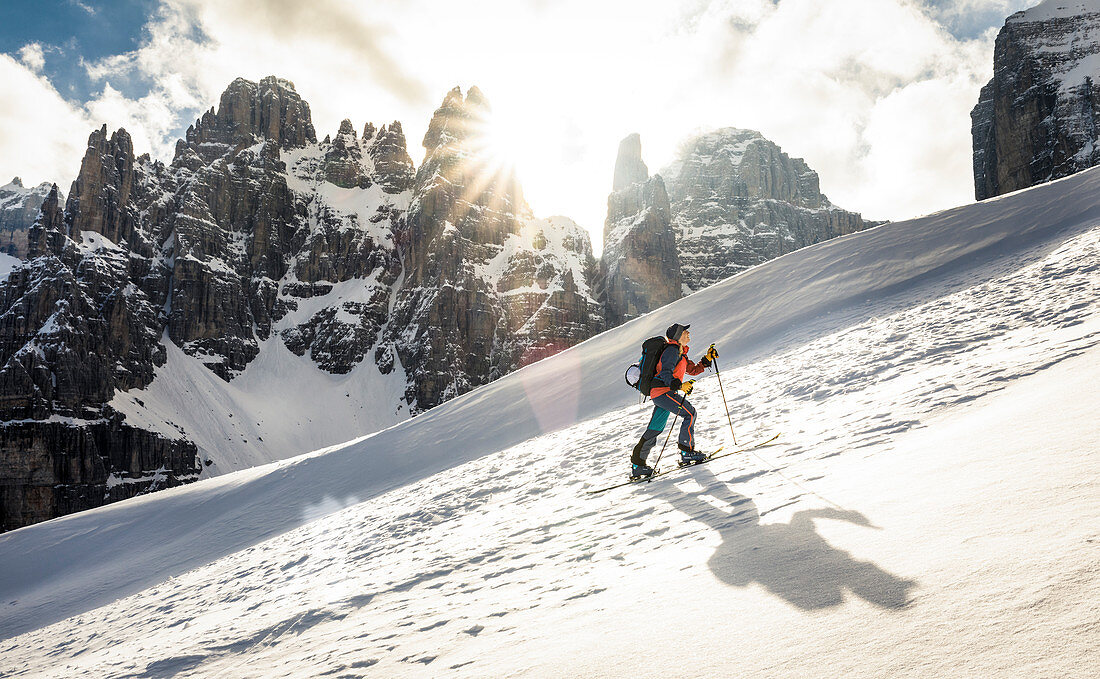 Skitourengeherin wirft Schatten im Aufstieg bei Gegenlicht, Brenta Gruppe, Italien