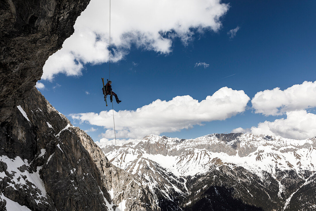 Alpinist rappels off an overhanging rock face with a ski on his backpack, Mieminger chain, Tyrol, Austria