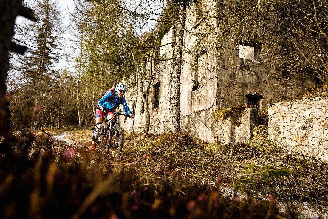 Young woman rides a mountain bike past a ruin, Lake Idro, Italy