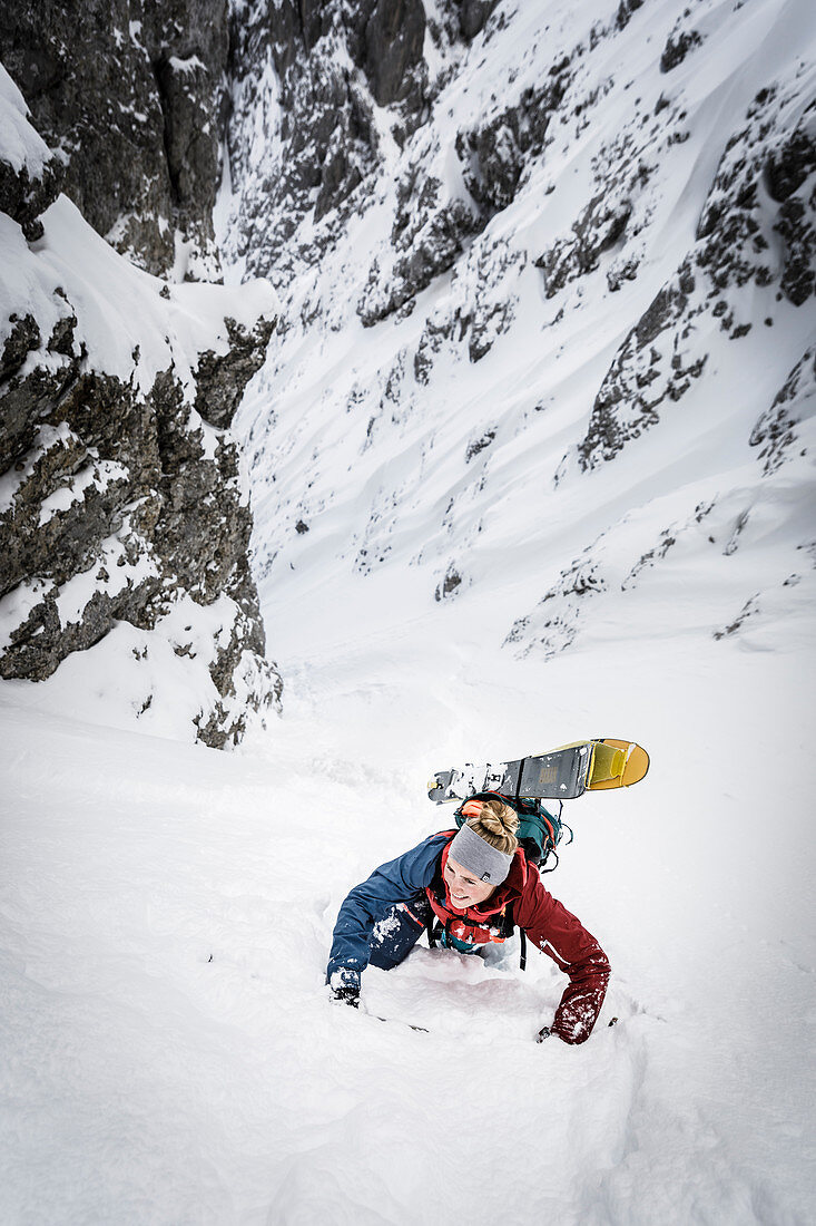 Skifahrerin im mühsamen Aufstieg durch eine steile Rinne zu Fuß, Wilder Kaiser, Tirol, Österreich