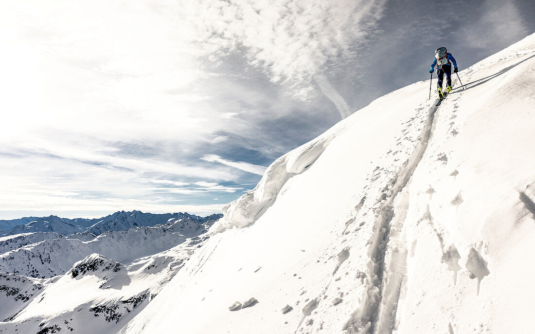 Skitourengeherin zieht eine steile Aufstiegsspur an einer Wechte vorbei richtung Gipfelkamm, Alpbach Tal, Tirol, Österreich