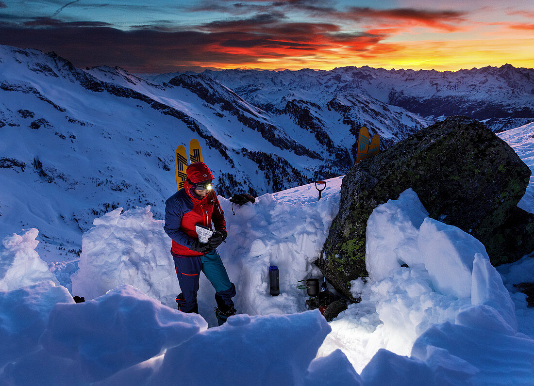 Junge Frau beim Auspacken einer Tüte Expeditionsnahrung beim winterlichen Biwakplatz, Valser Tal, Tirol, Österreich