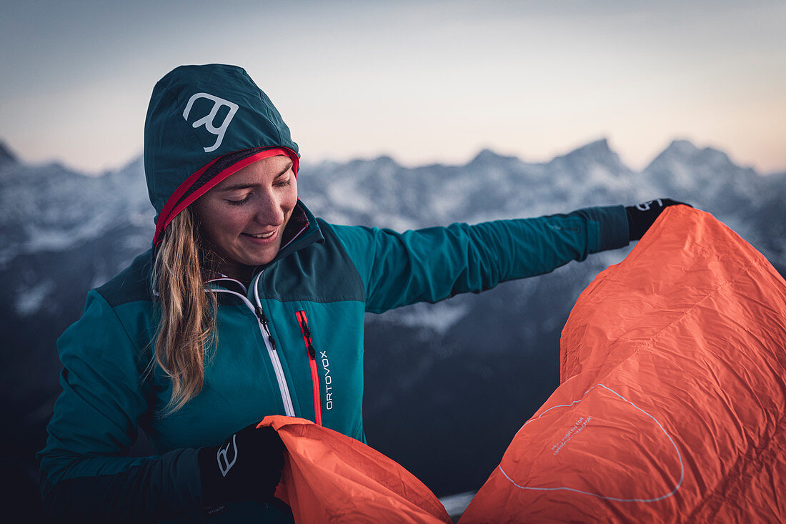 Young blonde woman prepares her bivouac sack in the evening light, Karwendel, Tyrol, Austria