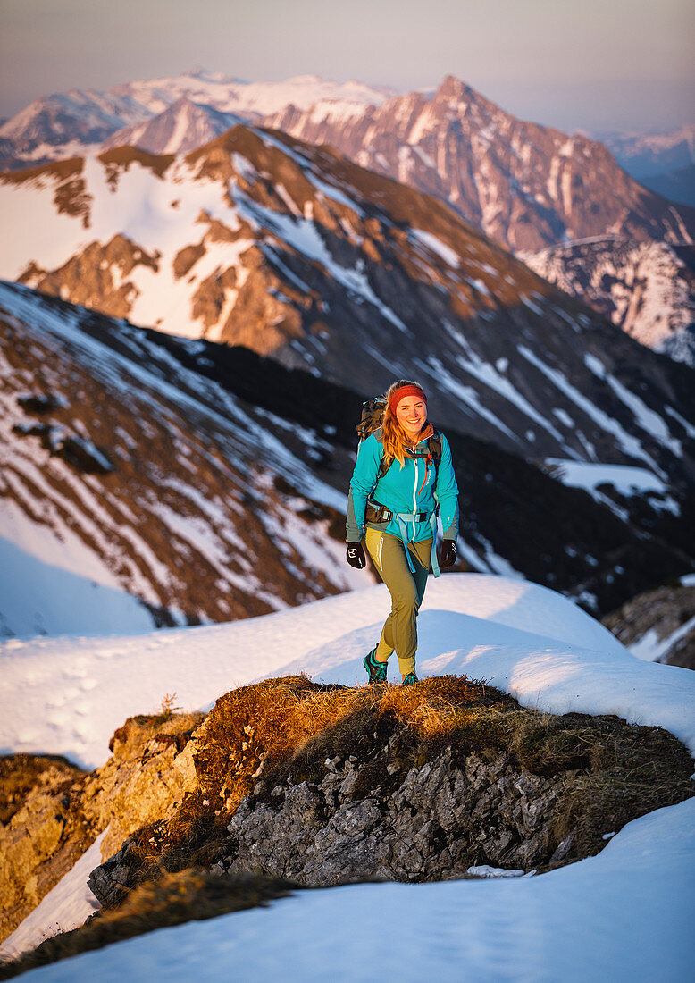 Junge Wandererin steigt im Abendlicht neben Schnee auf einem Rücken vor großartiger Karwendelszenerie, Hinterriss, Karwendel, Tirol, Österreich
