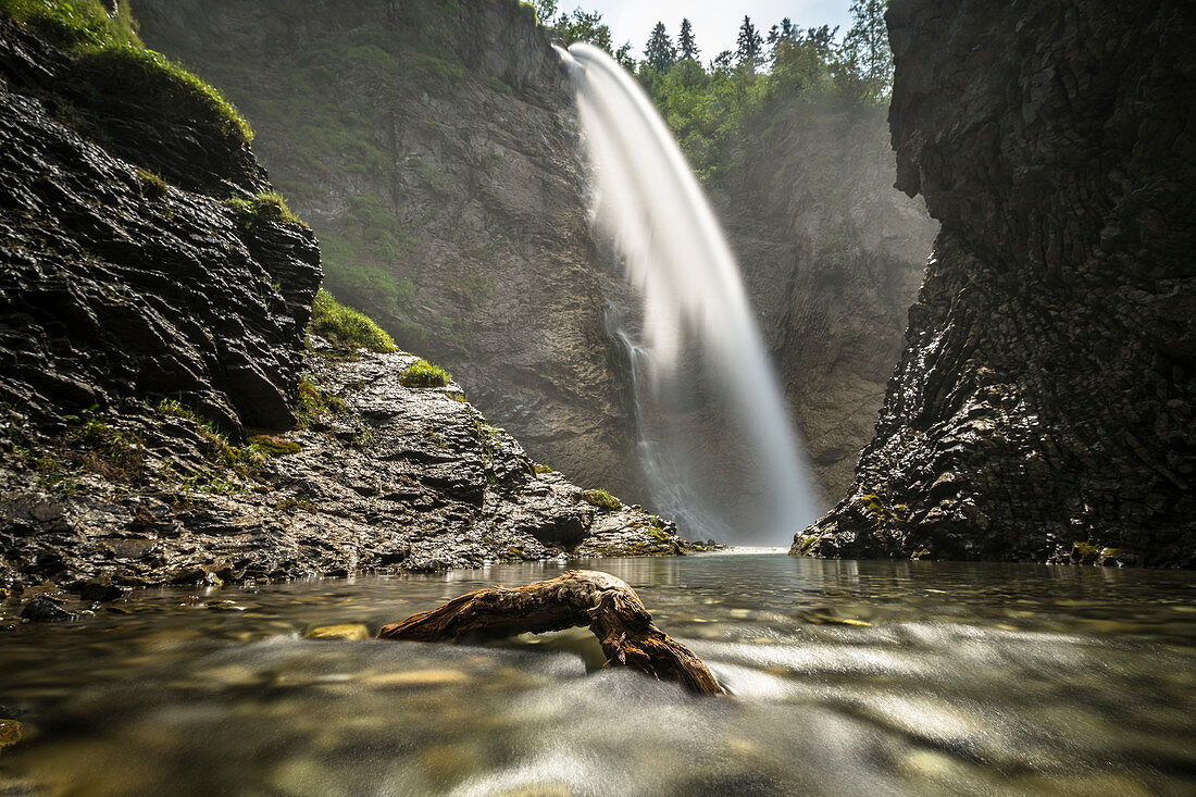 Berg Wasserfall in einer steinigen Schlucht mit Schwemmholz an einem Sommertag, Deutschland, Bayern, Oberallgäu