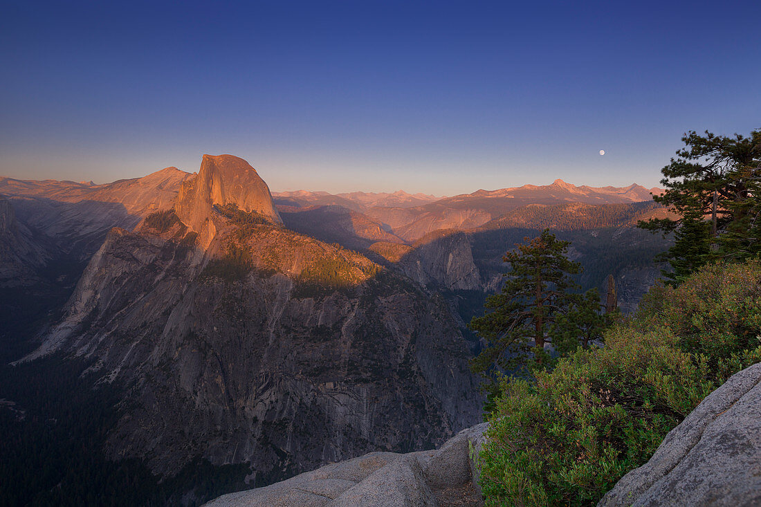 Half Dome im Yosemite Nationalpark angeleuchtet im Sonnenuntergang im Sommer, Mond am Horizont, USA\n