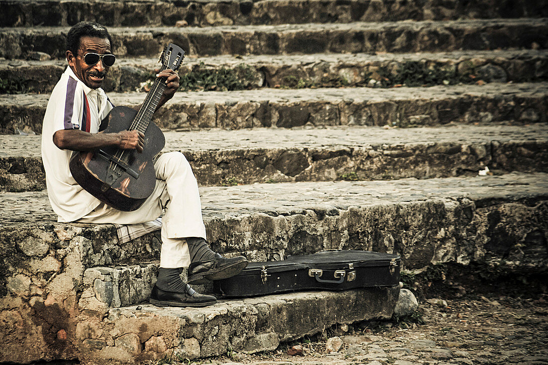 Ein Mann sitzt auf einer Steintreppe und spielt Gitarre. Trinidad, Kuba