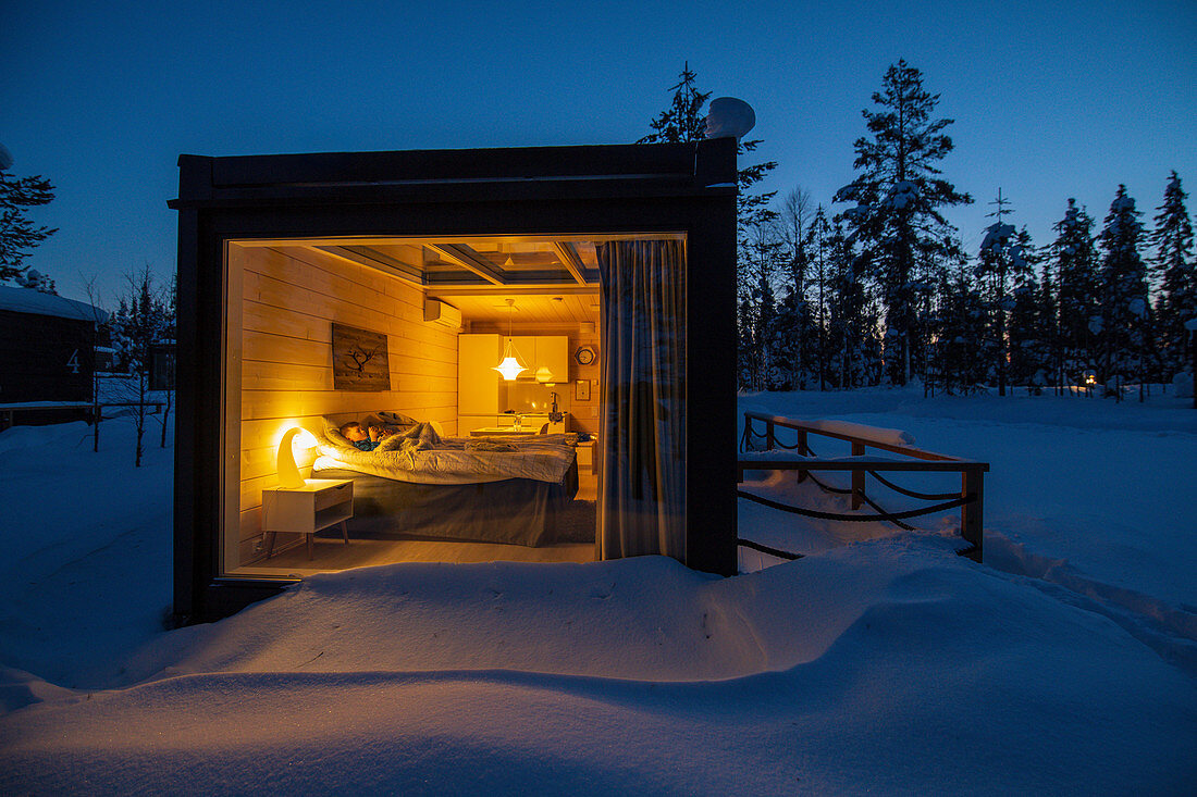 Blick in ein kleines beleuchtetes Ferienhaus im Winter, Urlaub in Finnland
