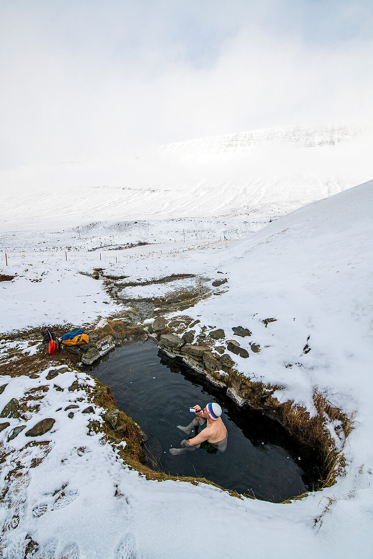 Abenteurer macht Pause und trinkt Bier in einer heißen Quelle, Winter in Island