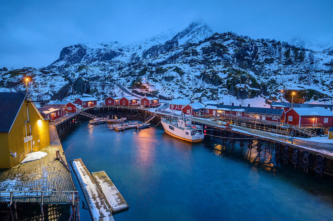 Beleuchteter Hafen von Nusfjord mit norwegischen roten Fischerhäusern, Nusfjord, Lofoten, Nordland, Norwegen