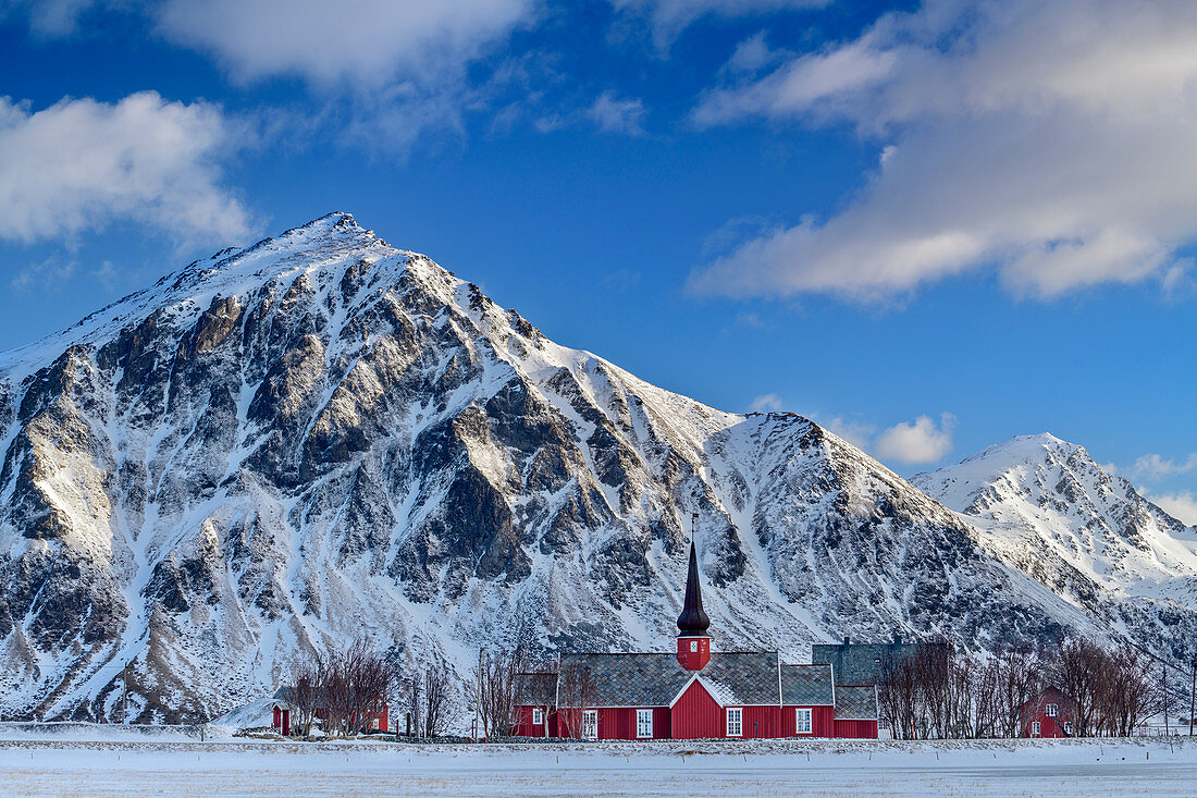 Rote Holzkirche von Flakstad mit verschneiten Bergen im Hintergrund, Lofoten, Nordland, Norwegen