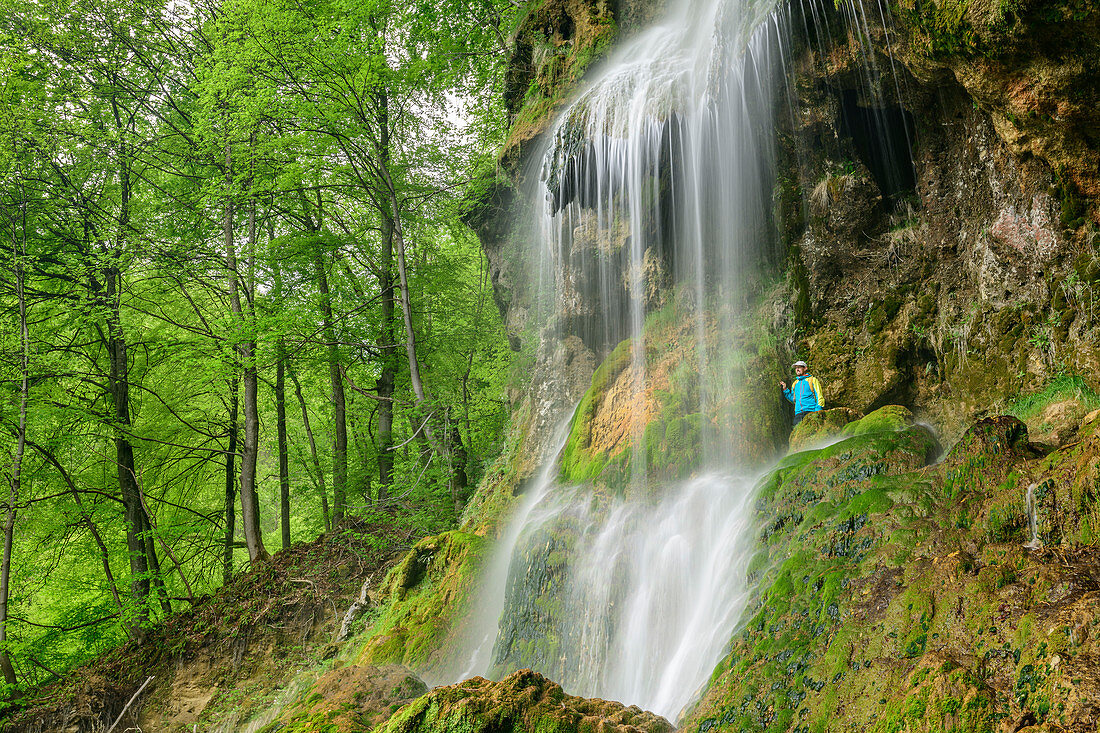 Hiker stands behind waterfall, Uracher Wasserfall, Bad Urach, Swabian Alb, Baden-Württemberg, Germany