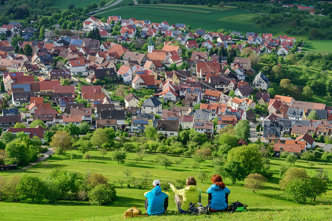 Three people sit in meadow and look at the village of Kohlberg, Jusiberg, Swabian Jura, Baden-Württemberg, Germany