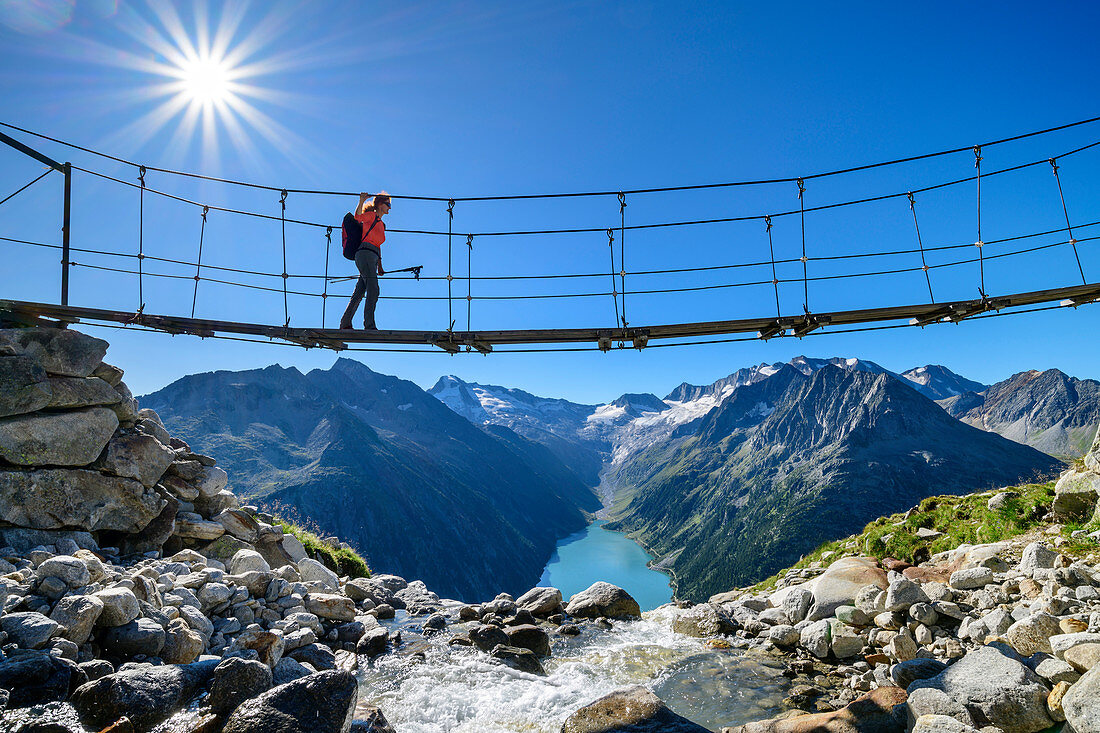 Frau geht auf Hängebrücke über Bach, Schlegeisspeicher und Großer Möseler im Hintergrund, Olpererhütte, Peter-Habeler-Runde, Zillertaler Alpen, Tirol, Österreich