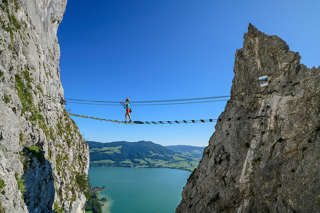 Frau geht auf Klettersteig über Hängebrücke, Klettersteig Drachenwand, Mondsee im Hintergrund, Drachenwand, Mondsee, Salzkammergut, Salzburg, Österreich