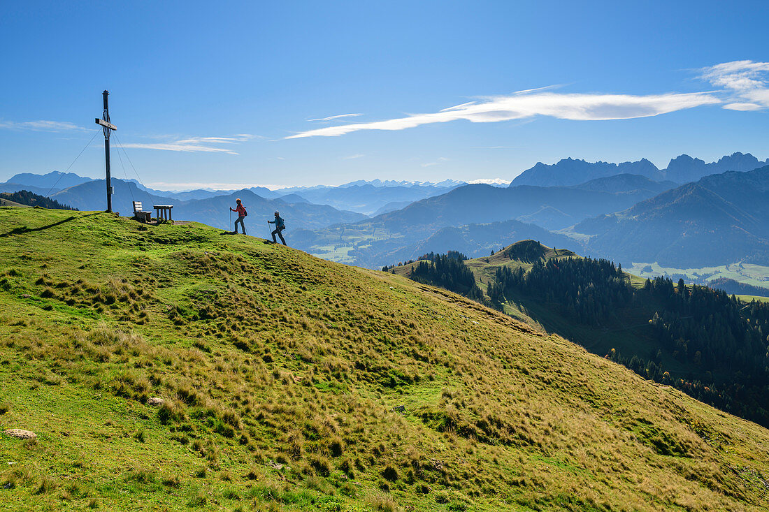 Zwei Personen beim Wandern steigen zu Gipfelkreuz auf, Kaisergebirge im Hintergrund, Wandberg, Chiemgauer Alpen, Tirol, Österreich 