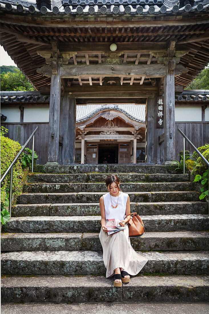 Japanese woman sitting on steps outside a Buddhist temple.
