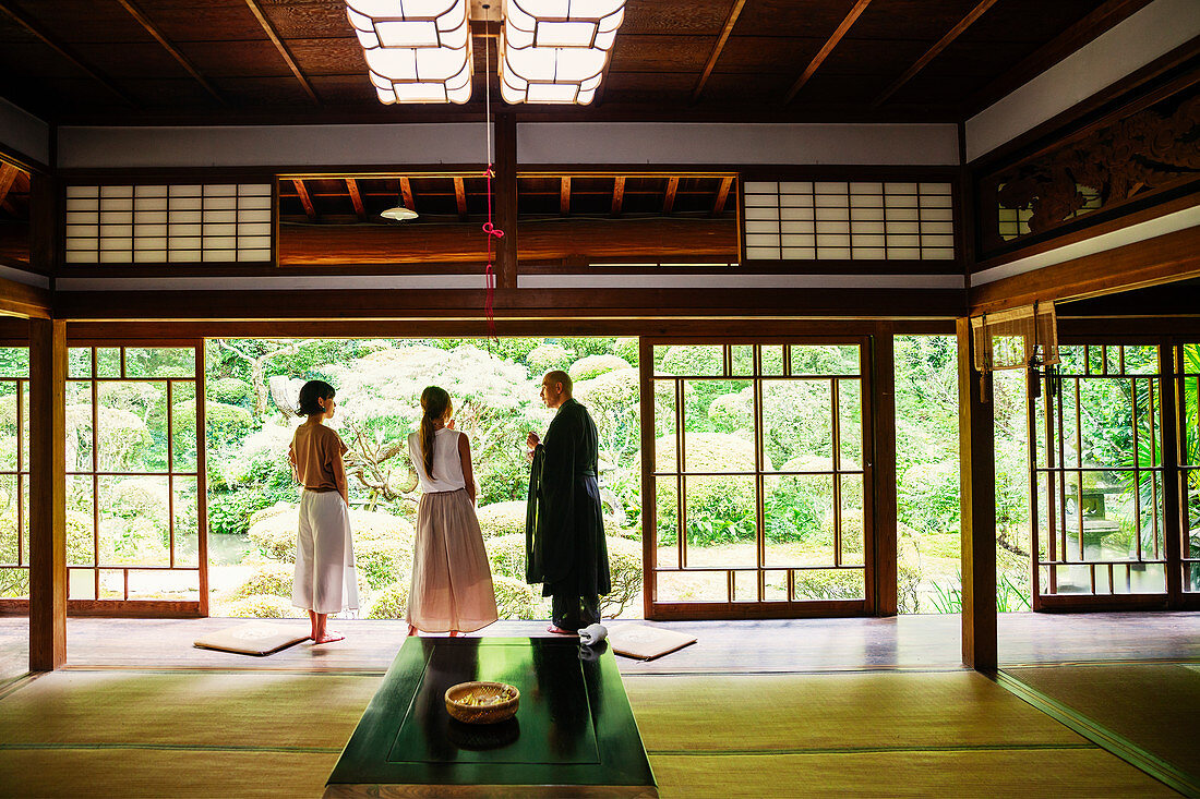 Buddhistischer Priester und zwei japanische Frauen stehen im einem buddhistischen Tempel