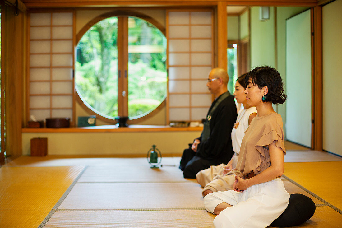 Zwei japanische Frauen und ein buddhistischer Priester knien und beten im buddhistischen Tempel