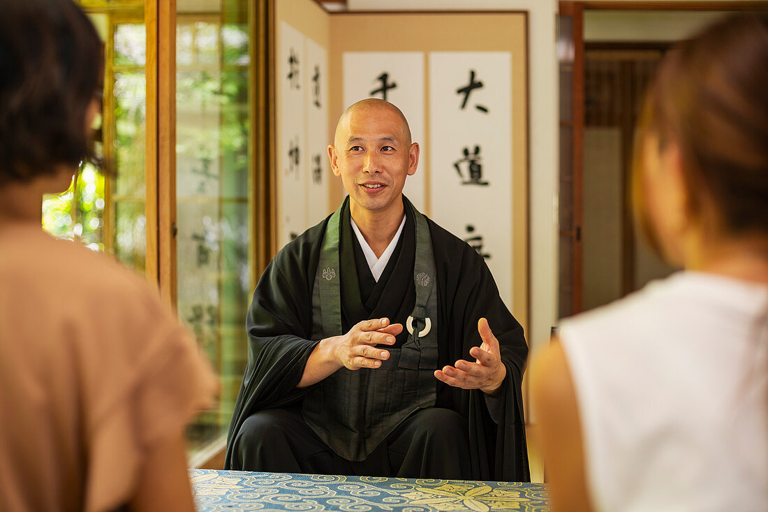 Zwei japanische Frauen und buddhistischer Priester knien und unterhalten sich im buddhistischen Tempel