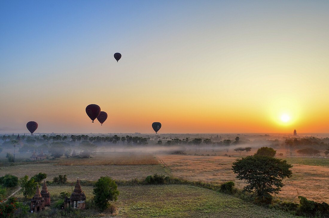 Heißluftballons über Landschaft mit entfernten Tempeln bei Sonnenuntergang, Bagan, Myanmar
