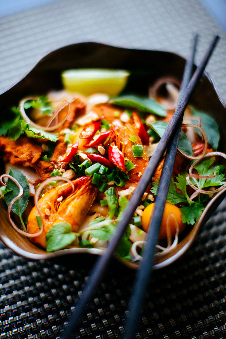 Asiatisches Essen mit Nudeln, Garnelen, Gemüse und Chili in einer Schale mit Essstäbchen