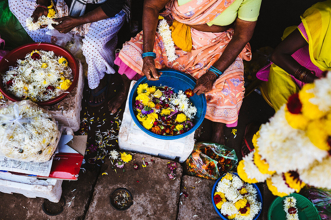 Frauen fädeln auf einem Markt Blumen auf