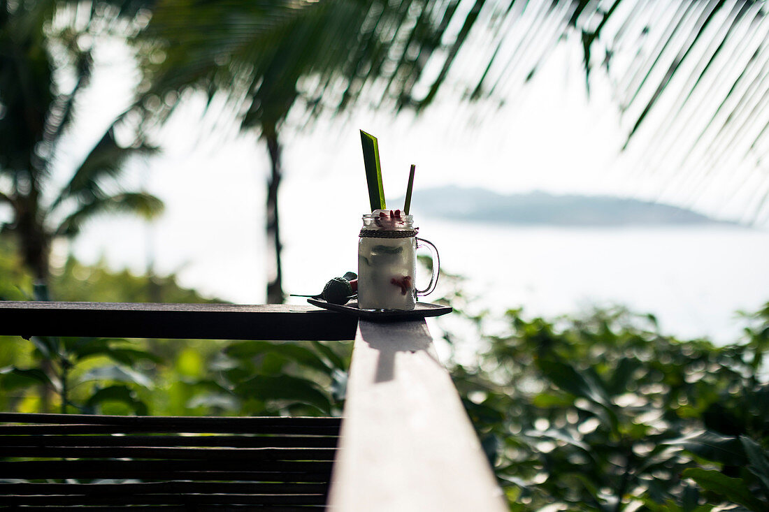 Close up of a "Tom Yum" cocktail with coconut-infused liquour standing a balustrade of balcony.