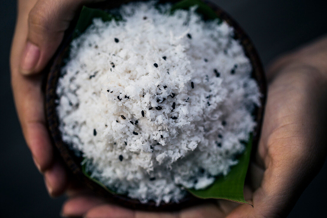 High angle close up of hand holding coconut flesh and black sesame seeds used as a body scrub.