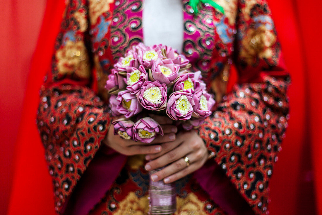 Close up of young Vietnamese bride wearing a colourful robe, holding a bouquet of lotus flowers.