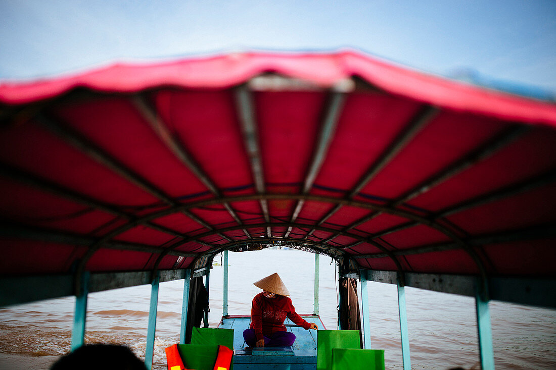Woman piloting a boat with red canopy through a river.