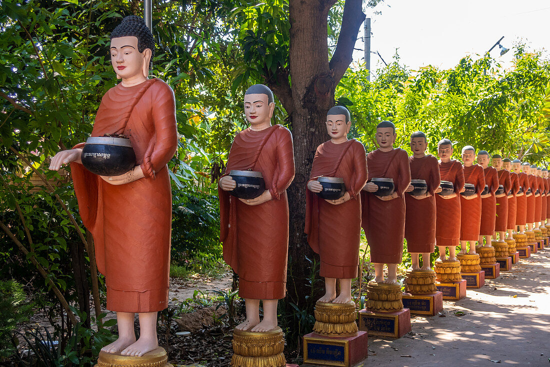 Reihe buddhistischer Mönchsstatuen mit roten Gewändern und Almosenschalen in den Gärten des buddhistischen Tempels in Siem Reap