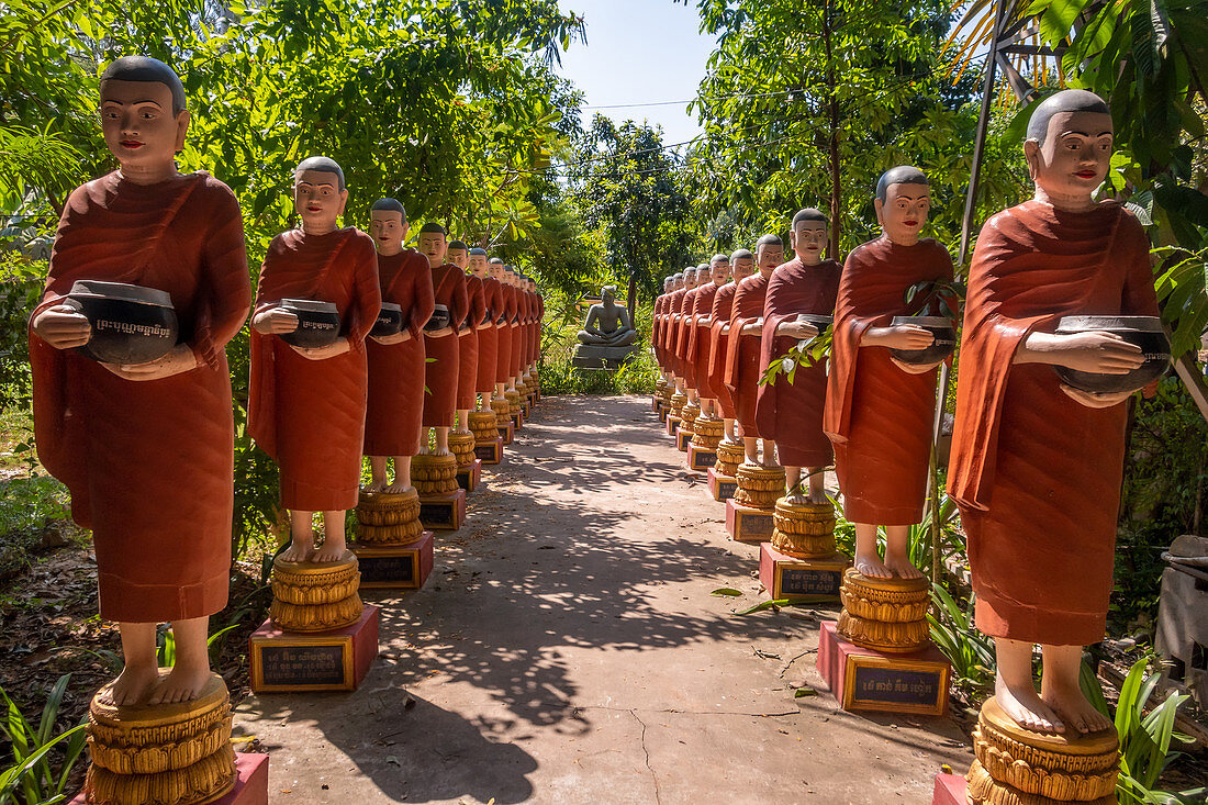 Row of Buddhist monk statues with red robes and alms bowls in the gardens of the Buddhist Temple at Siem Reap