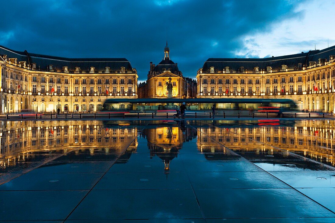 France, Gironde, Bordeaux, area listed as World Heritage by UNESCO, Bourse Place, La Lune harbour, Night view of a tram passing a historic building and their reflections on an esplanade water