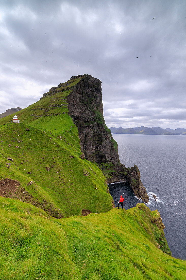Hiker on cliffs looking to Kallur Lighthouse, Kalsoy Island, Faroe Islands, Denmark, Europe
