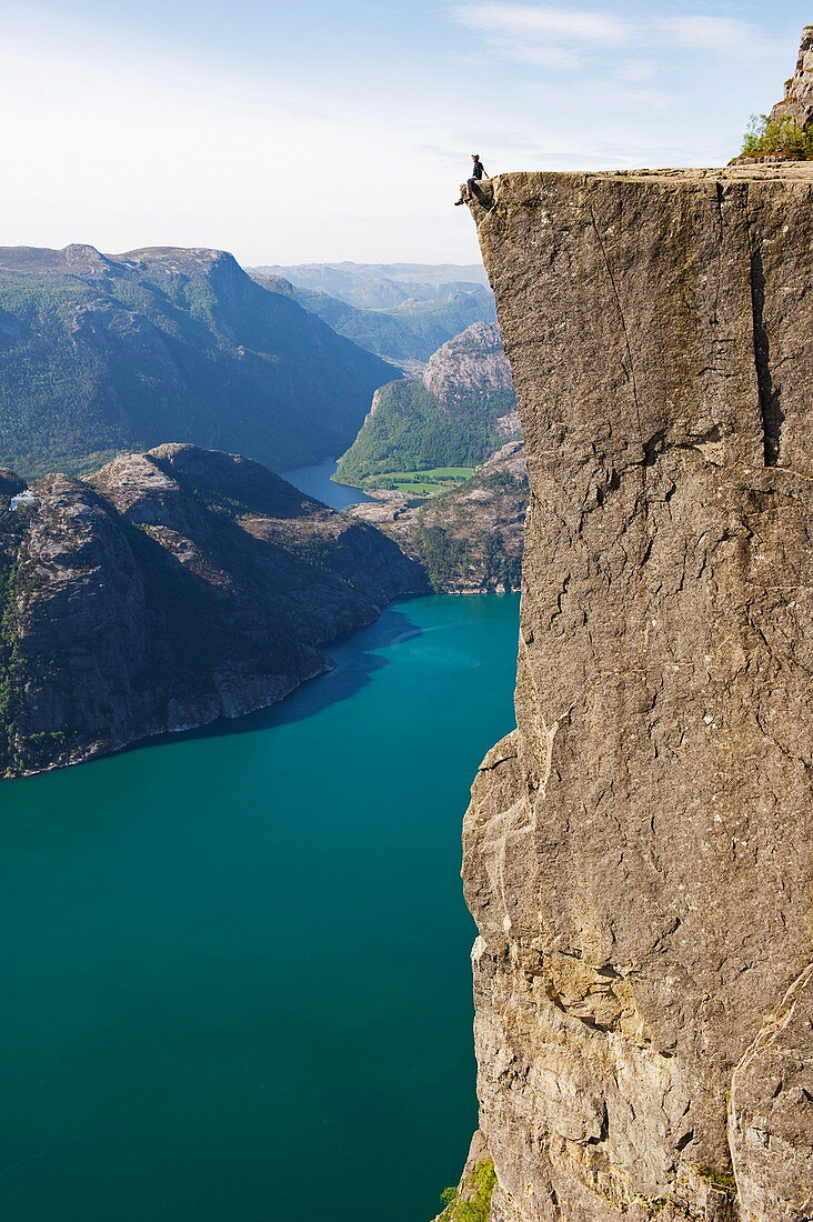 Mann sitzt auf Preikestolen (Kanzelfelsen) über dem Fjord, Lysefjord, Norwegen, Skandinavien, Europa