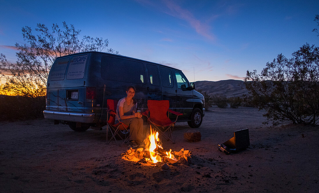 Woman by the campfire and van on the sand dunes of Kelso in the Mojave National Park at sunset