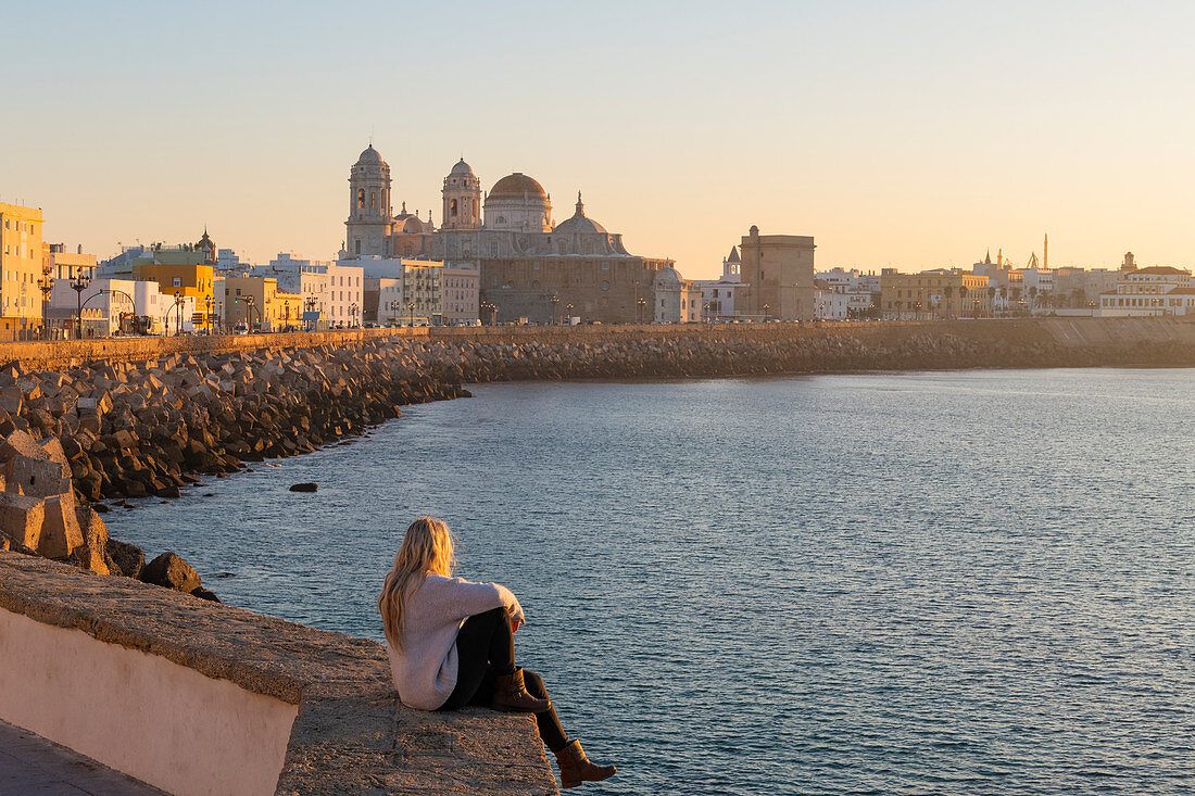 Woman enjoying the view of Santa Cruz Cathedral and ocean seen from the promenade along quayside, Cadiz, Andalusia, Spain, Europe
