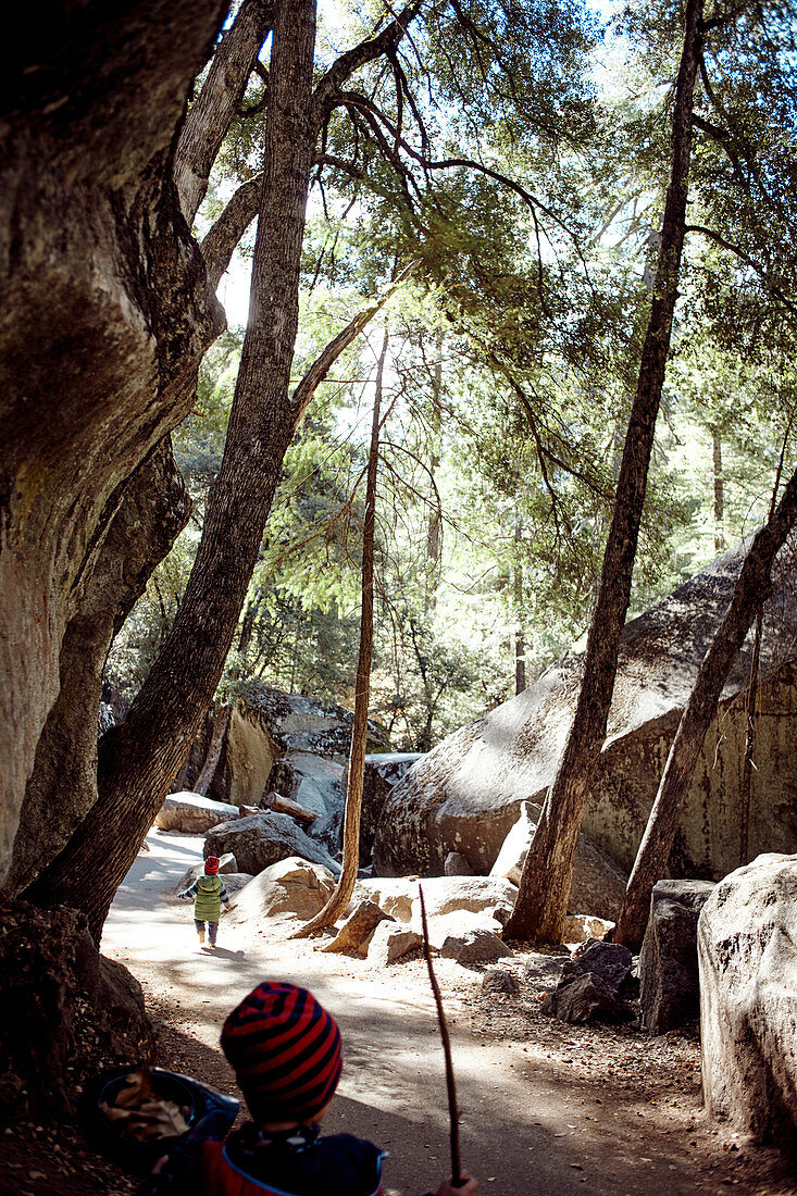 Children run on a hiking trail past rocks in Yosemite Park. California, United States.