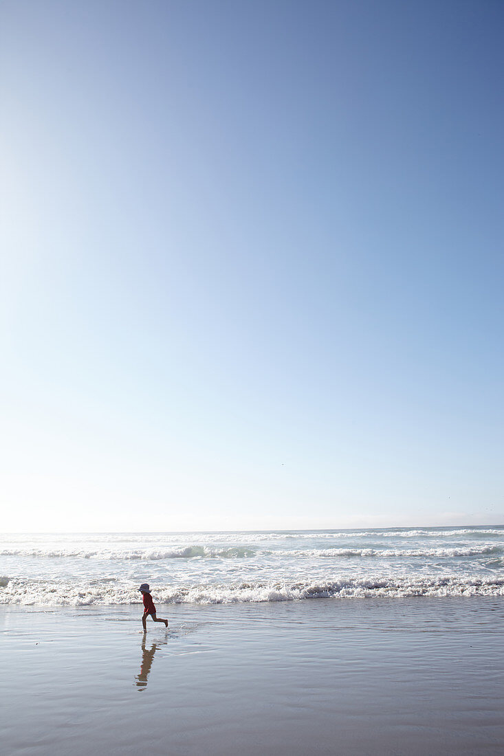 Kind läuft mit den Wellen am Strand von Big Sur, Kalifornien, USA