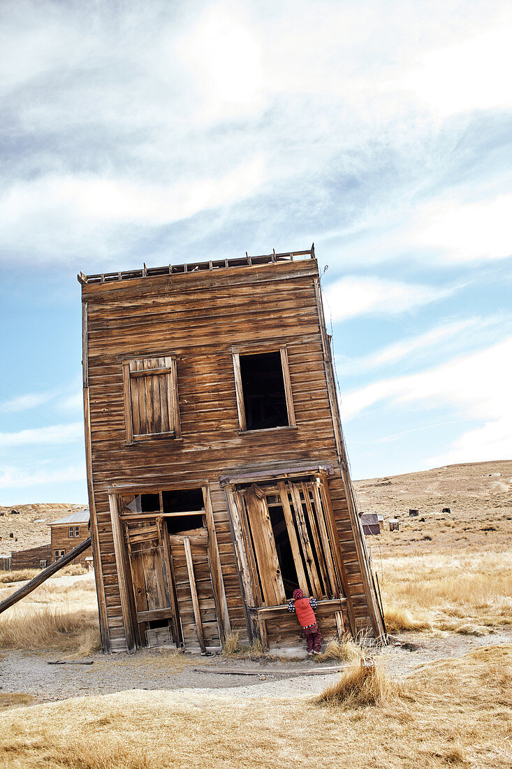 Child looks through a window into a skewed house in the ghost town of Bodie. Eastern Sierra, California, United States.