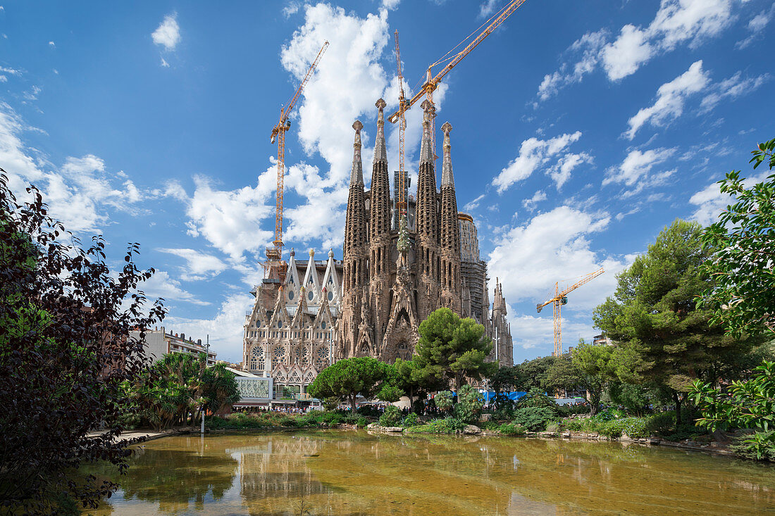 Kathedrale von Gaudi Sagrada Familia von außen mit Spiegelung im Wasser bei Sonne, Barcelona, Spanien\n