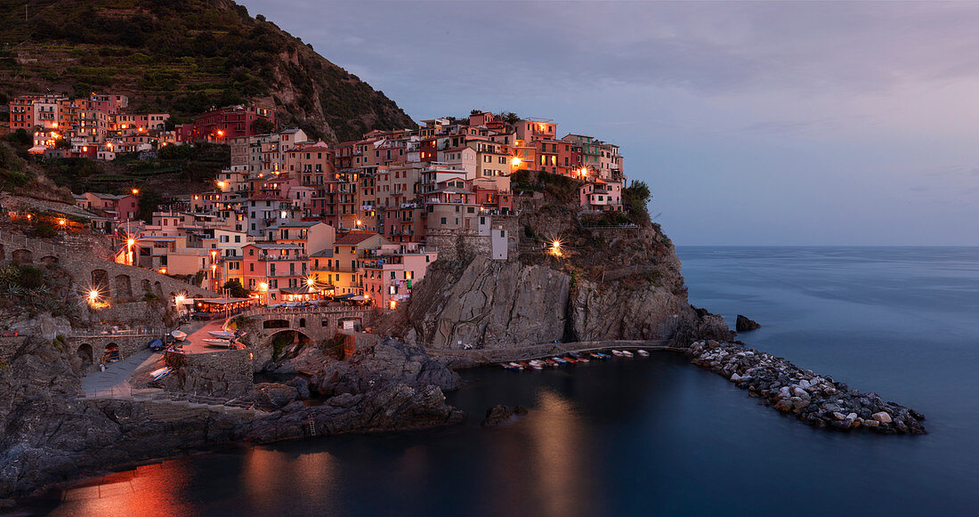 Bucht in Cinque Terre mit Dorf Manarola am Abend mit Lichtern, Italien\n