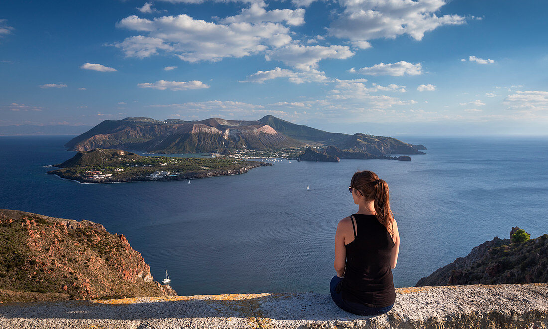 Küste von Lipari mit Frau sitzend, Blick auf Vulkaninsel Vulcano am Tag, Sizilien, Italien