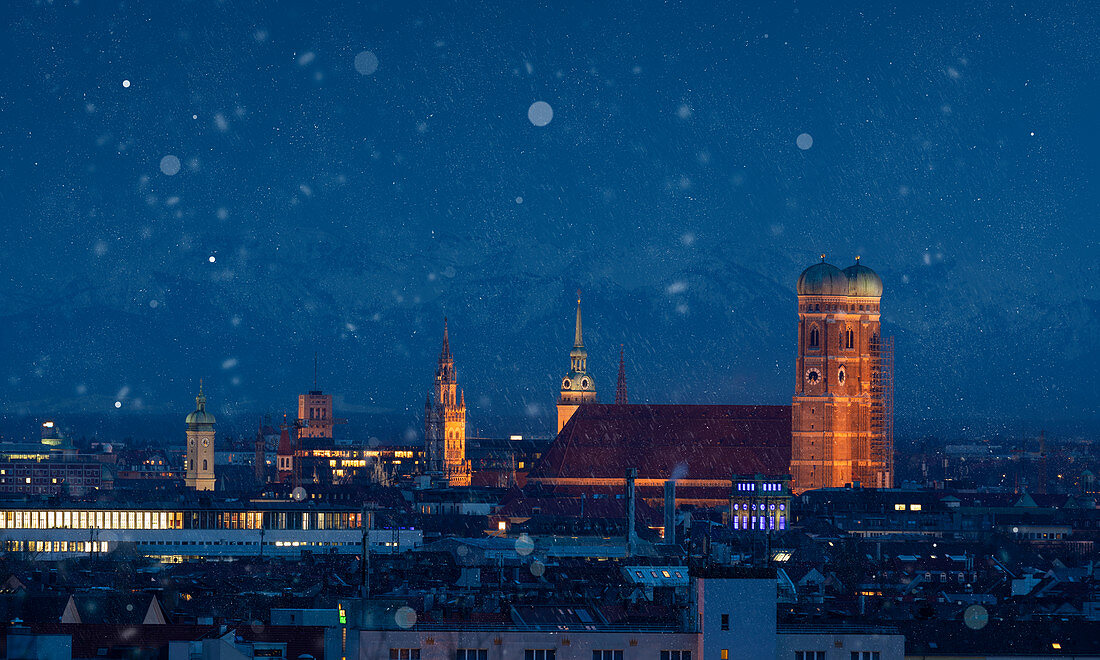 Munich city skyline with illuminated Frauenkirche during snowfall at night