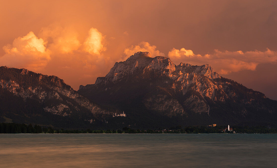 Neuschwanstein Castle and Hohenschwangau on Forggensee in the Ammer Mountains with clouds at sunset, Bavaria
