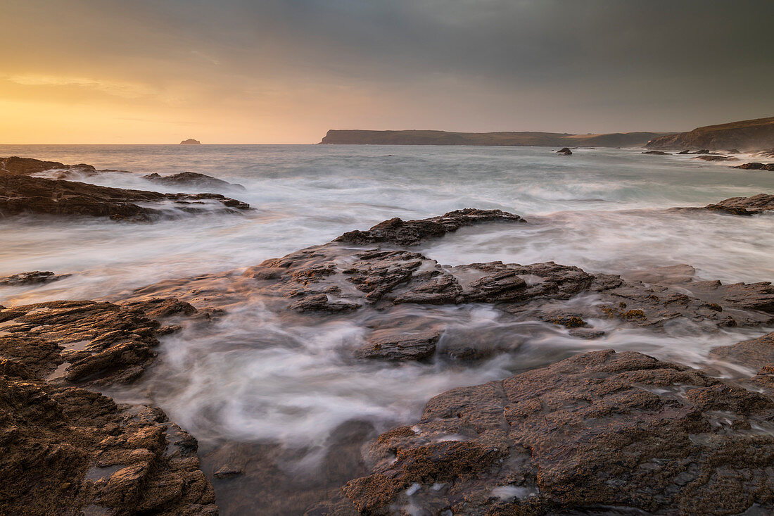 Wellen über Felsvorsprünge bei Sonnenuntergang an der Nordküste von Cornwall, Cornwall, England, Vereinigtes Königreich, Europa