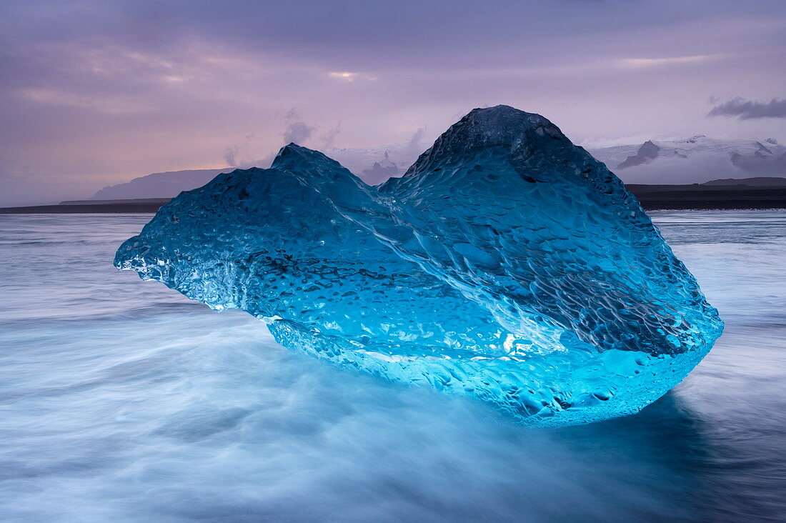 An den schwarzen Sand von Breidamerkursandur gespülter, durchscheinender, blauer Eisberg in der Nähe der Gletscherlagune von Jokulsarlon, Ostisland, Polarregionen